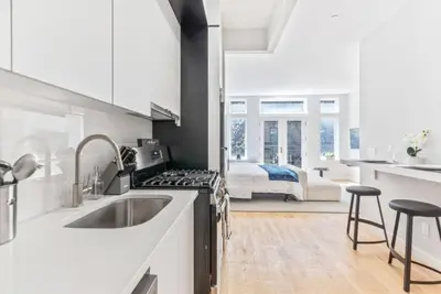 a white kitchen with a sink and a bedroom at Studio w Charming Juliet Balcony in Upper East in New York