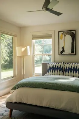 a bedroom with a bed with a ceiling fan and two windows at Stunning All-Season Renovated Barn Escape! in East Chatham