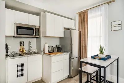a kitchen with white cabinets and a table and a refrigerator at 73-1406 New 1BR 1Bth UWS Doorman Gym in New York