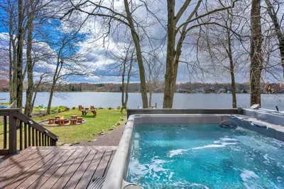 a hot tub on a deck with a view of a lake at Pet Friendly! Lakefront w Hot Tub, Firepit! in Tobyhanna