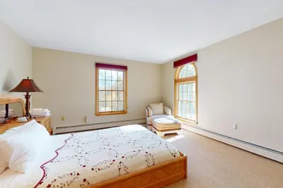 a bedroom with a bed and a chair and two windows at Green Mountain Sunrise in Dover