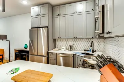 a kitchen with white cabinets and a stainless steel refrigerator at Walk to Journal Square Modern Apt about 4 Mi to NYC! in Jersey City