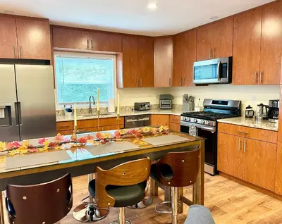 a kitchen with wooden cabinets and a large island with bar chairs at Saugerties Waterfront Getaway in Saugerties