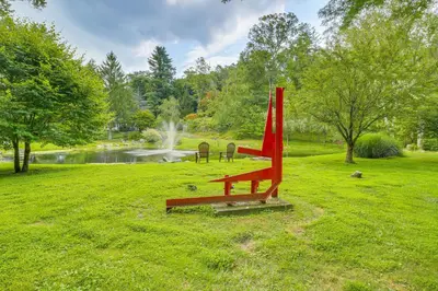 a red bench in a park with a pond at Serene Holmes Cottage Near Lakes and Trails! in Pawling