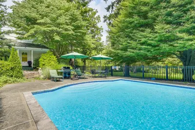 a swimming pool with chairs and umbrellas in a yard at Serene Holmes Cottage Near Lakes and Trails! in Pawling