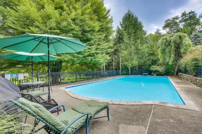 a swimming pool with chairs and an umbrella at Serene Holmes Cottage Near Lakes and Trails! in Pawling