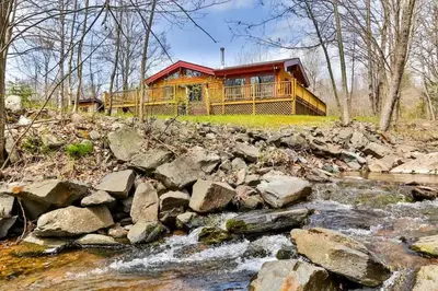 a log home with a creek in front of it at 4 Bedroom Log Cabin with Stream and Great Location in Lanesville