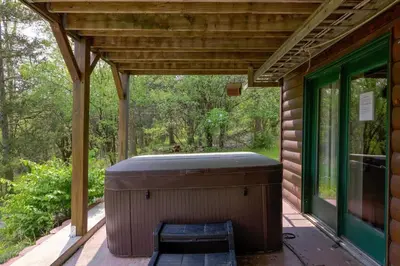 a covered porch with a hot tub and a bench at Cozy Athens Cabin on the Lake with Hot Tub & Backyard in Athens