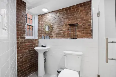 a bathroom with a white toilet and a brick wall at Vintage Luxe NY - Designer Lofts & Apartments NYC in New York