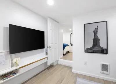 a white living room with a flat screen tv on a wall at Pelham Haven Suite in New York in Pelham