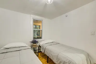 two beds in a white room with a window at NYC Area Apartment on Hudson River! in Hastings-on-Hudson