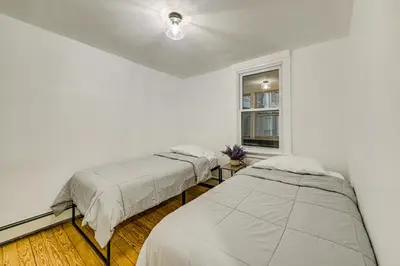 two beds in a white room with a window at NYC Area Apartment on Hudson River! in Hastings-on-Hudson