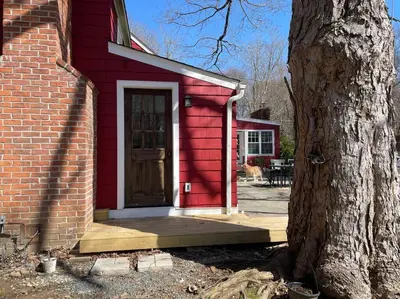 a red house with a door next to a tree at The Hideaway in Brewster
