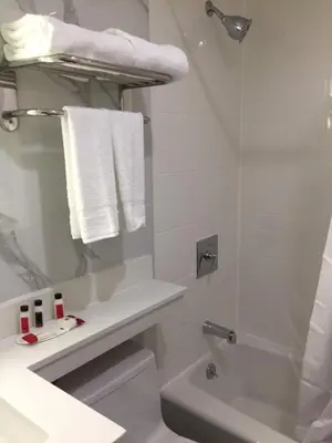 a white bathroom with a shower and a toilet and a sink at Voyage Hotel in Long Island City