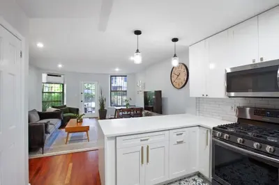 a kitchen with white cabinets and a living room at Charming Central Park Townhome in New York