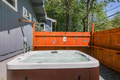a hot tub in a backyard with an orange fence at COZY COTTAGE Spacious 4Bdrm 2Bth, Hot Tub, Game Movie Room, Close to camelback skiing, Sauna Firepit, Arcades, Backyard Playground, 2 Min Walk To Pool, Lake, Beach, Basketball in Tobyhanna