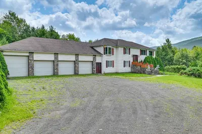 a white house with two garage doors on a driveway at 3 Mi to Colgate Lake Mtn-View Home, Deck and Grill! in East Jewett