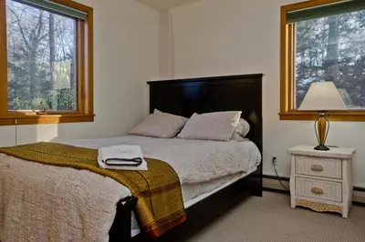 a bedroom with a bed and a lamp and two windows at Amherst Woodland Escape in Amherst