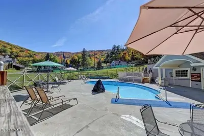 a swimming pool with chairs and an umbrella at 2 BR Condo Mountain Views At Jiminy Peak- Sleeps 7 in Hancock