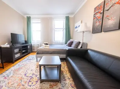 a living room with a black leather couch and a tv at Bright Studio in Central NYC in New York