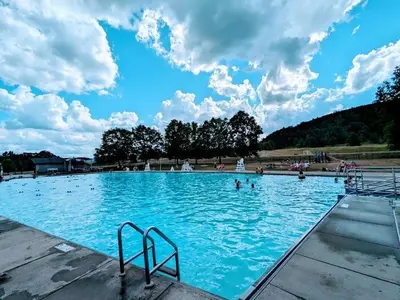a large blue swimming pool with people in it at Modern Pine Tree Chalet with HOT TUB, Outdoor TV, VIEWS, Games & POOL 5 mins away!! in Gilboa