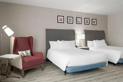 a hotel room with two beds and a red chair at Hilton Garden Inn Lenox Pittsfield in Pittsfield