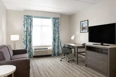 a living room with a couch and a desk with a television at Hilton Garden Inn Lenox Pittsfield in Pittsfield