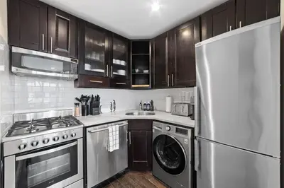 a kitchen with wooden cabinets and a stainless steel refrigerator at Chelsea Vista II by Rove Travel 2BR PH with Rooftop in New York