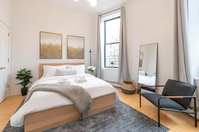 a bedroom with a large bed and a chair at Cypress Court I by Rove Travel 2BR Harlem Apartment in New York