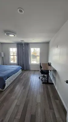 a bedroom with a bed and a desk and two windows at 3 Bedroom Renovated Model House in New Hyde Park