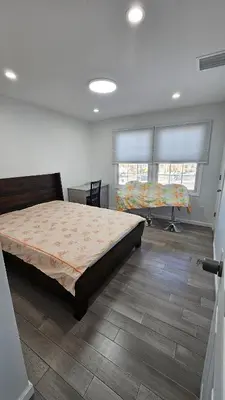 a bedroom with a bed and a desk and two windows at 3 Bedroom Renovated Model House in New Hyde Park
