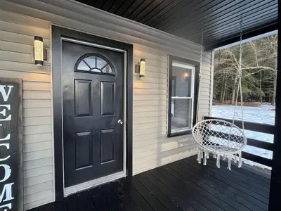 a porch with a black door and a swing at Twin Pines Lake Resort 1 in Northville