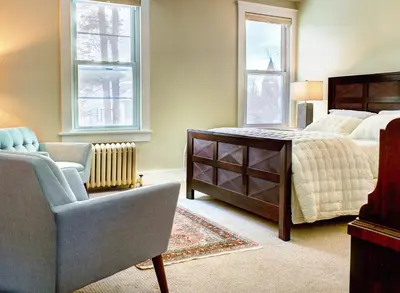 a bedroom with a bed and a chair and windows at Gateways Inn in Lenox