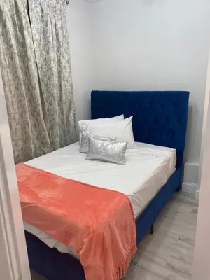 a small bed with a blue headboard and pillows at Adam Clayton Apartment in New York