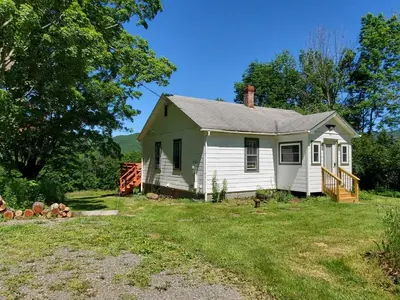 a small white house on a grass field at Pleasant Brook Cottage in Roxbury