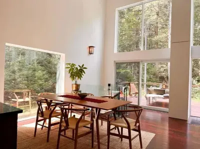 a dining room with a table and chairs and windows at Unique and Private 25ft Waterfall House in Hunter in Elka Park