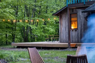 a cabin in the woods with a porch and two benches at Chic Catskills Cabin with Hot Tub and Fire Pit in Lanesville
