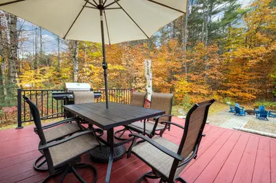 a table and chairs on a deck with an umbrella at 3BR Lake Luzerne Retreat with Game Room & Cozy Fire Pit in Lake Luzerne