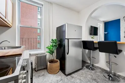 a kitchen with a refrigerator and two black chairs at Spacious 2BR on the Upper East Side Steps from Central Park in New York