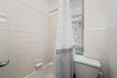 a white bathroom with a toilet and a window at Spacious 2BR on the Upper East Side Steps from Central Park in New York
