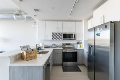 a kitchen with white cabinets and a stainless steel refrigerator at Chique Loft 10 Min from NYC with Gym, Pool & Sauna in Jersey City