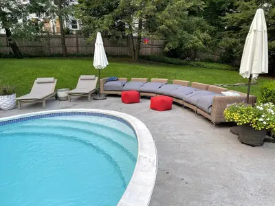 a couch and chairs next to a pool with umbrellas at The Historic Jesse Buel Farmhouse w Heated Pool in Albany