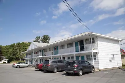 a white building with cars parked in a parking lot at Lake George Residence LLC in South Glens Falls