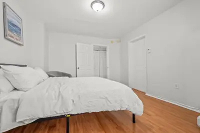 a white bedroom with a bed and a wooden floor at Spacious 3-Bedroom Apartment near NYC - 15min to Times Square, Empire State Building, Central Park, Statue of Liberty in Jersey City