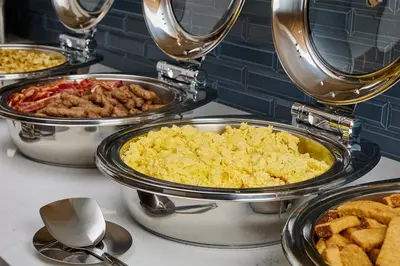 a buffet of different types of food in pans at Hyatt Place Secaucus Meadowlands in Secaucus