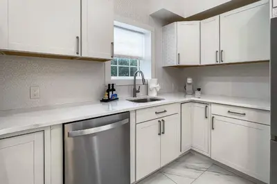a kitchen with white cabinets and a stainless steel dishwasher at Cozy Cottage in Cos Cob in Greenwich