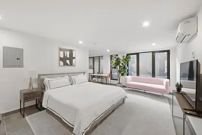 a white bedroom with a bed and a pink chair at 149 Green Street in Brooklyn