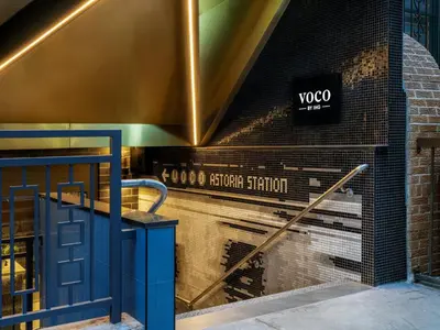 a sign on the side of a brick building with a blue door at voco Astoria by IHG in New York