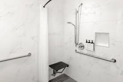 a bathroom with a shower with a bench in it at voco Astoria by IHG in New York