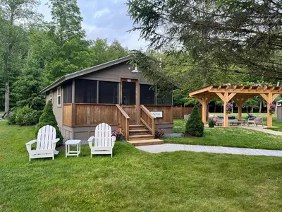 two white chairs sitting in the grass in front of a house at Antrim Streamside in Livingston Manor